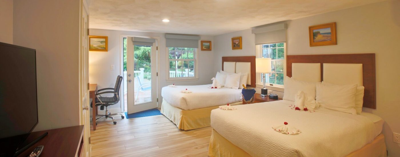 Large studio bedroom with two queen beds in white linens, bright windows and writing desk with lamp