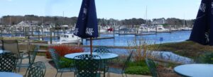 Outdoor patio dining at Brax in Harwich with Saquatucket Harbor views, docked boats, and blue water on a clear Cape Cod day.