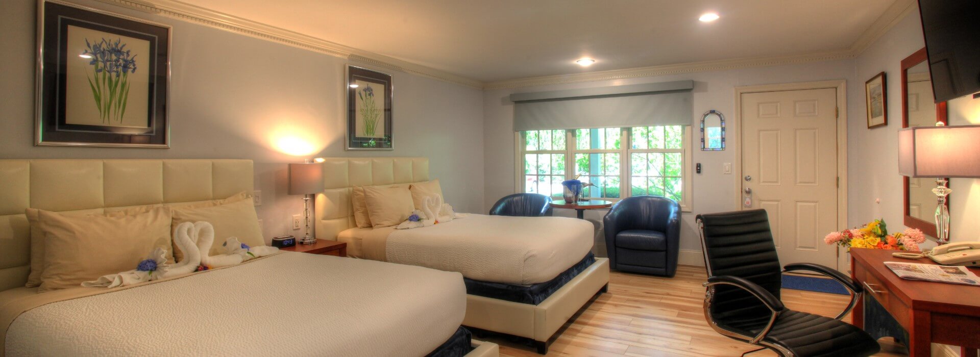 Spacious hotel room with queen bed, large french doors and sitting chair next to table with vase of flowers