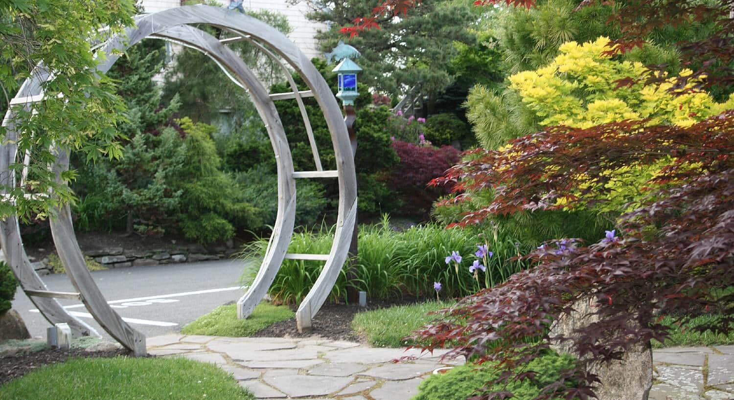 Circular wooden gate at the end of a stone sidewalk surrounded by colorful plants and bushes