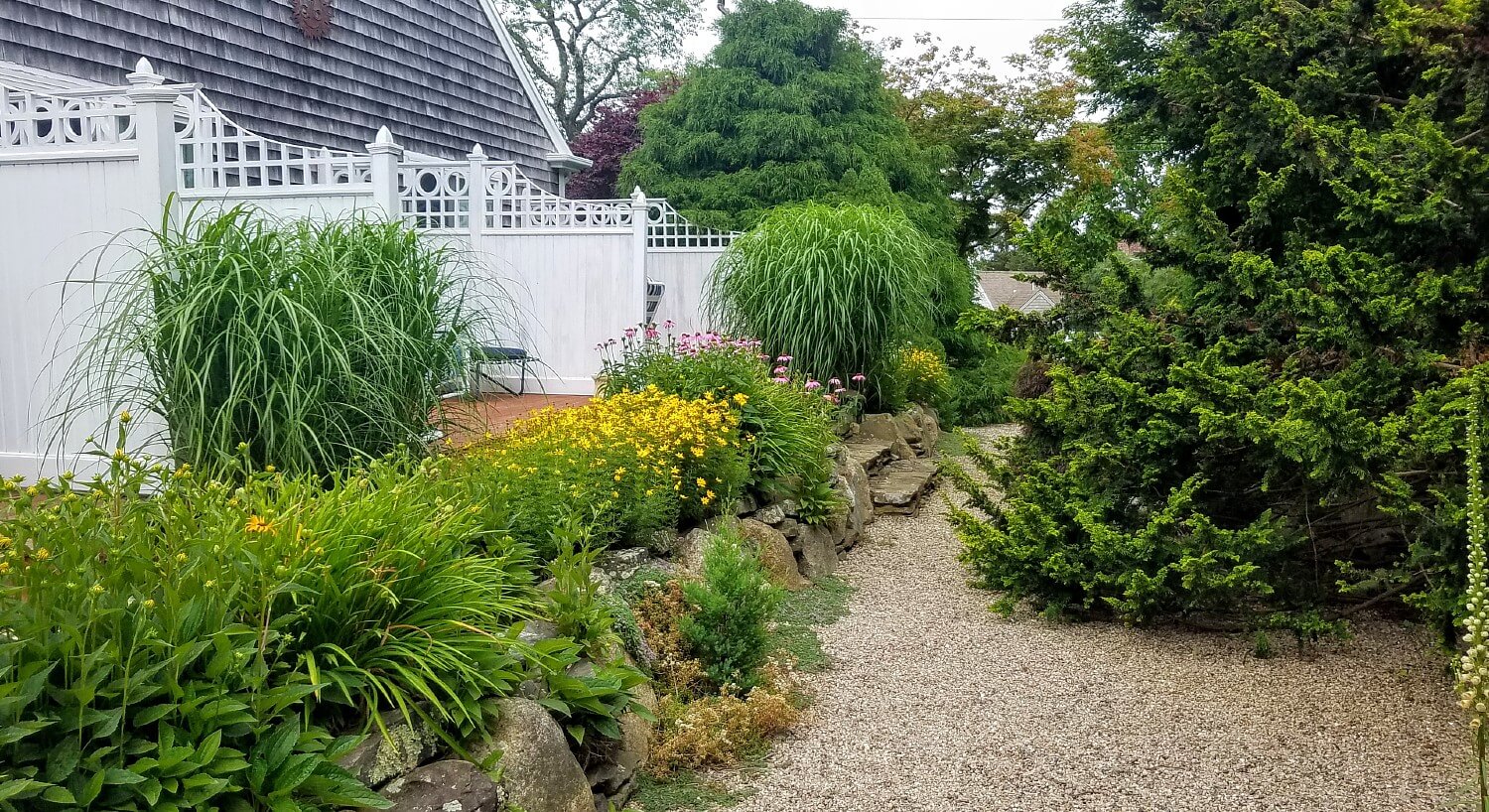 Backside of a row of hotel rooms with private patios, white divider fences and lush trees and flowering plants