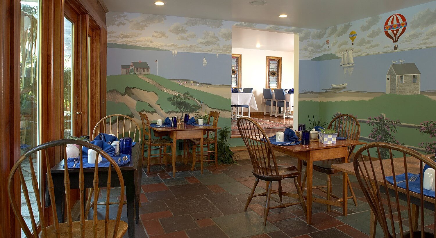 Dining area with murals on the walls, large windows, and four tables of two set for breakfast