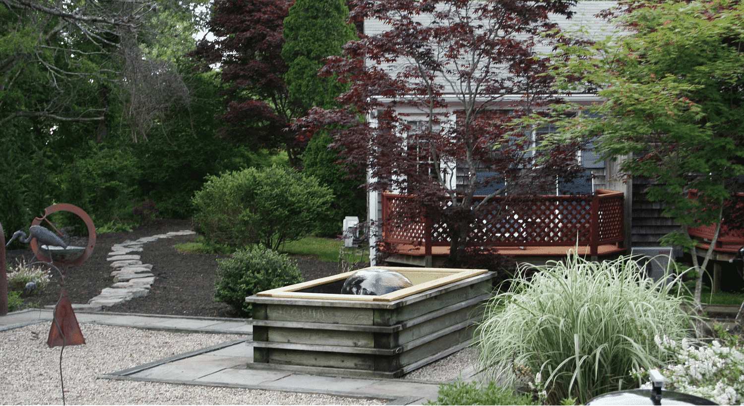 Back deck area of a cottage with water fountain feature, metal sculpture and rock patio