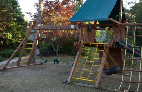 Outdoor wooden play structure for kids with rope ladders, slide and three swings