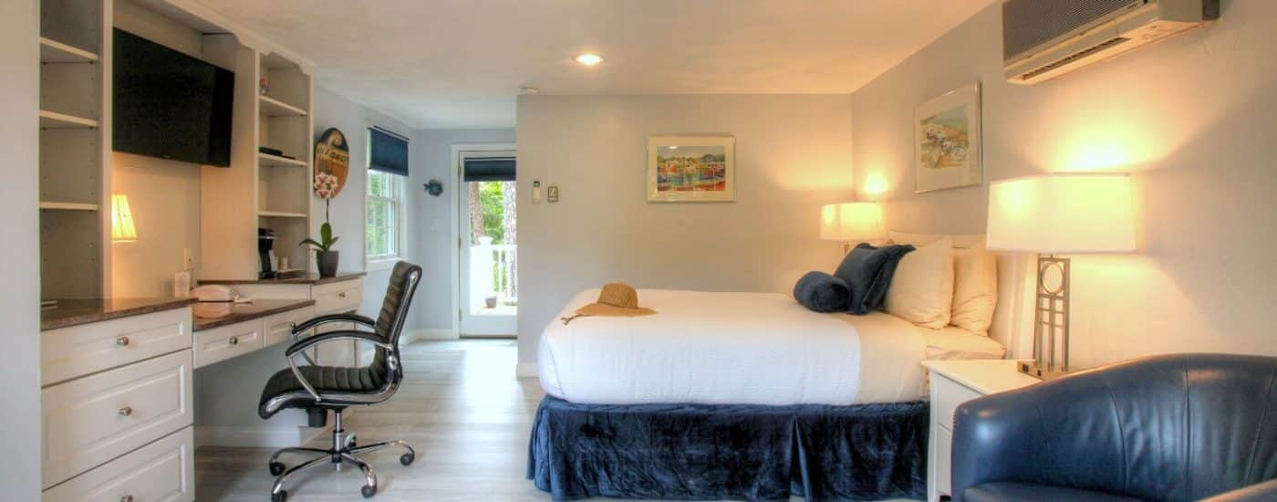 Bright guest room with queen bed, off white walls, light grey flooring, large windows blue leather chairs