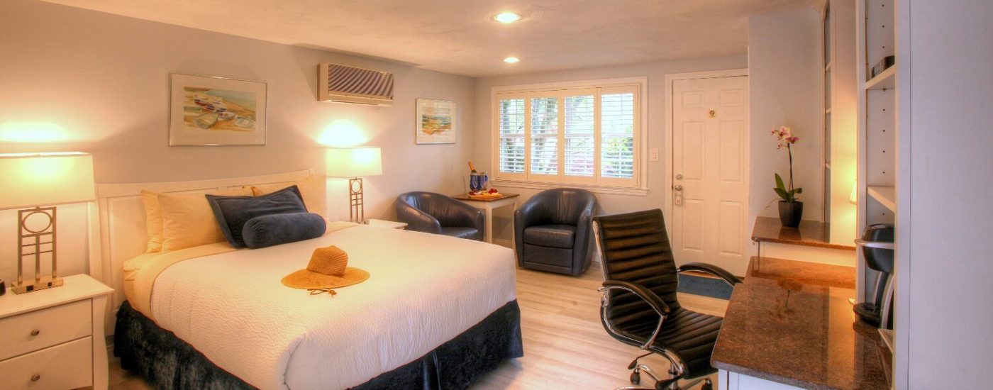 Bright and airy bedroom with white walls, queen bed, desk and hutch with TV and blue leather sitting chairs