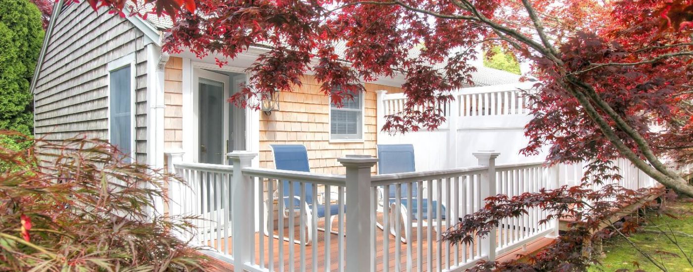 Back deck of a private hotel room with white railings, sitting chairs and surrounded by trees and green plants