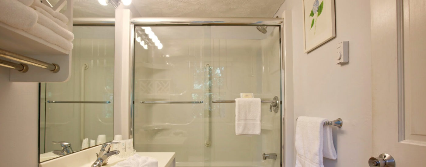 White bathroom with glass doors to the bathtub/shower, and white counter sink.