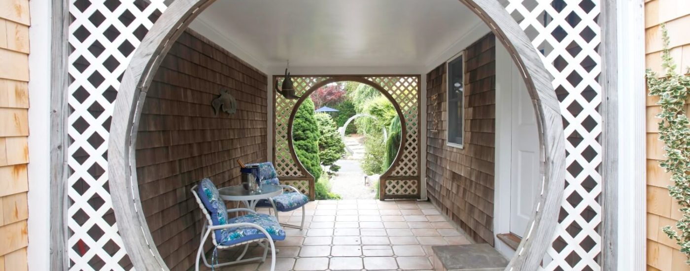 Breezeway with table & chairs and several circular arches along a path lined with trees and plants