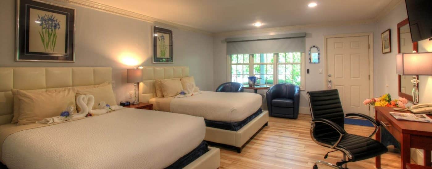 Bedroom with two queen beds, leather club chairs under a large window and writing table underneath a hung TV