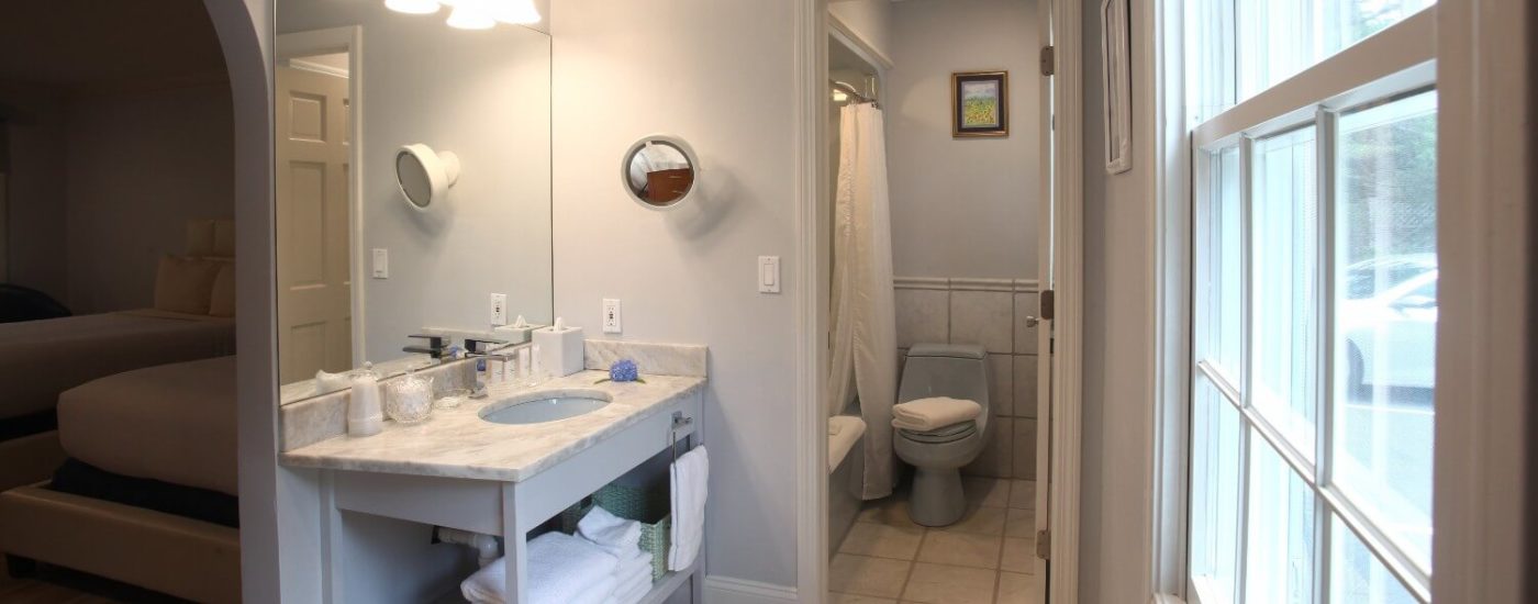 Bright bathroom with a marble sink top, stone floor and large window with a blind.