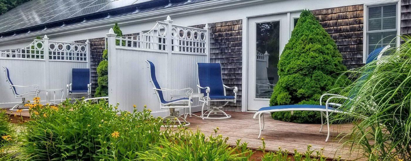 Outdoor decks separated by white privacy fences with sitting chairs and surrounded by lush green plants and shrubs