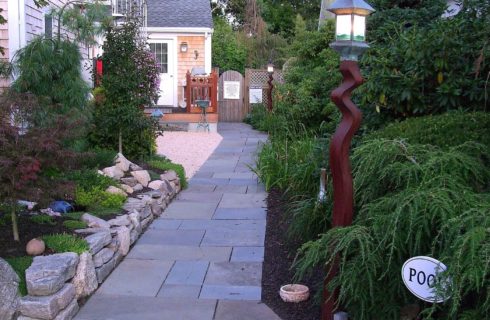 Stone patio next to outdoor building surrounded by lush landscaping and sign pointing to the pool