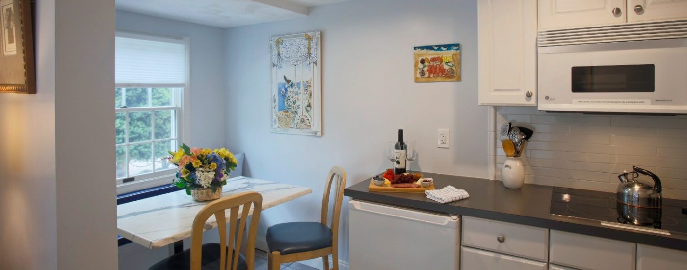 Bright kitchen with large window, marble table & wood chairs, white kitchen cabinets and black countertop.