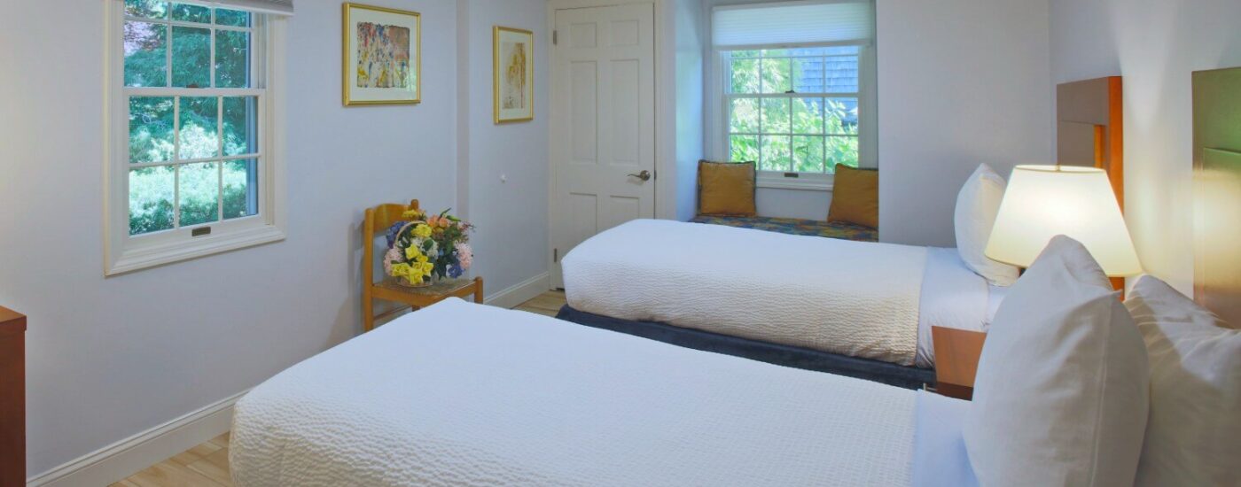 Bedroom with two twin beds, each under a bright window with one dresser and mirror