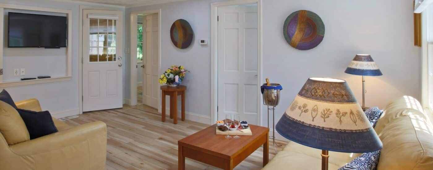 Cottage living room with two cream leather couches, coffee table and kitchenette behind a half wall