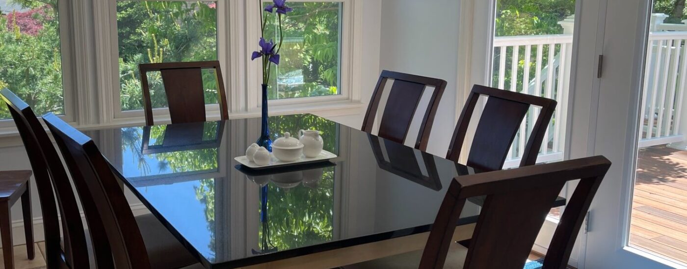 Small dining table set with four chairs in a room with bright windows and door open to a deck with flowers