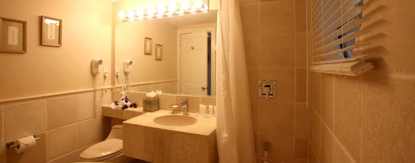 Beige bathroom with marble tiled wall around bathtub and window, tile sink with large mirror.