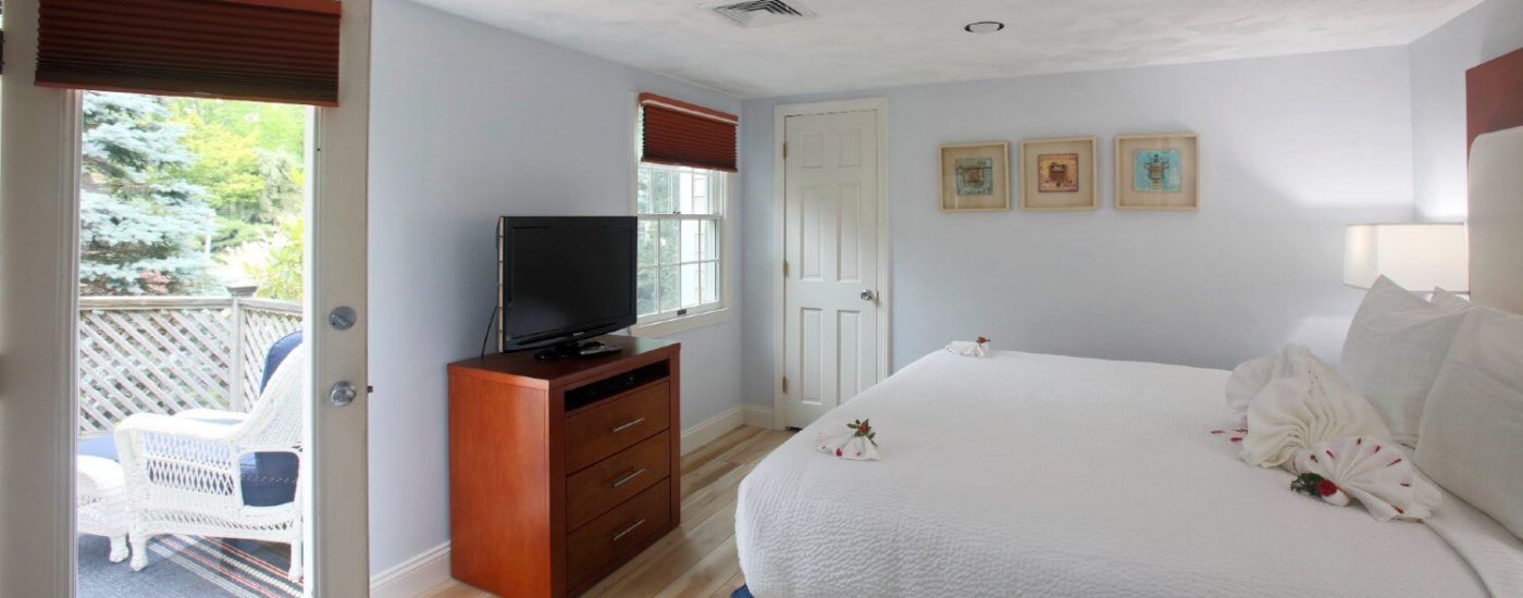 Bright bedroom with queen bed, dresser with flat screen tv & glass door to outdoor deck with patio furniture.