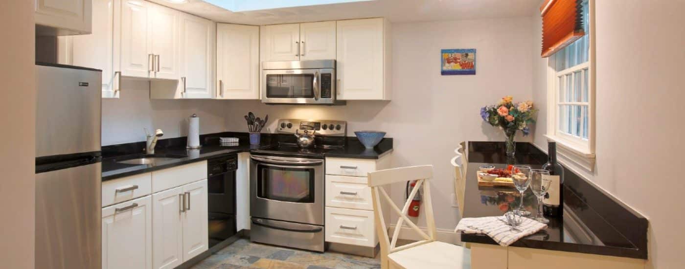 Kitchen with black countertop, white cabinets, a skylight and large window, and bar counter with chairs and wine glasses.