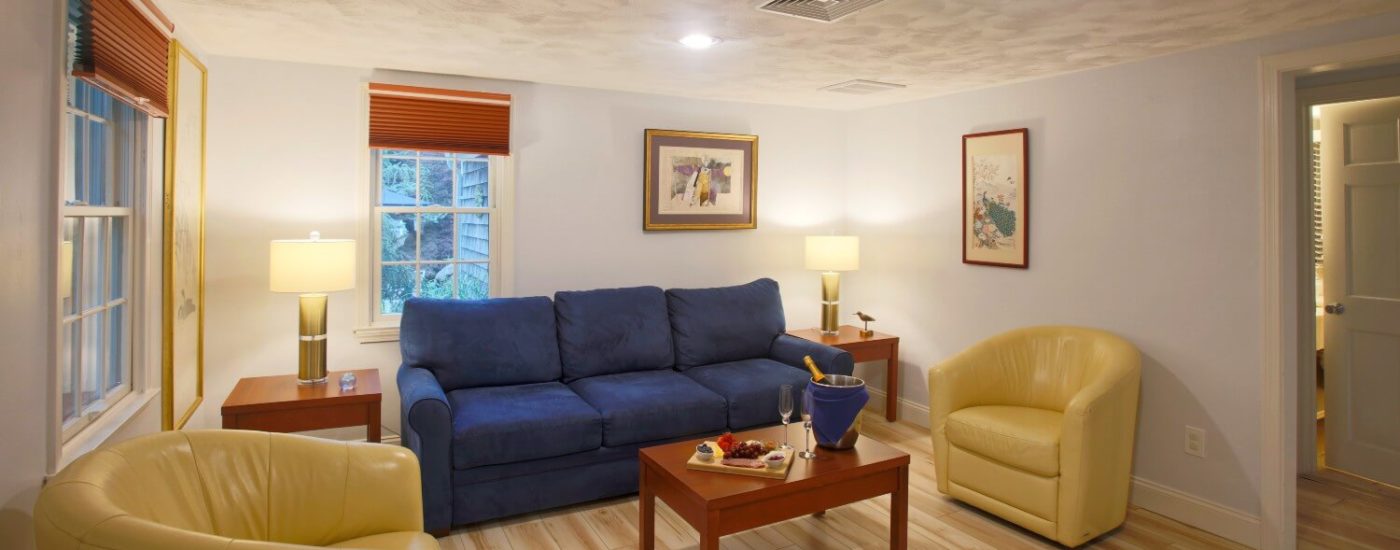 Bright living room of a cottage with blue couch, yellow leather chairs, coffee table and light wood flooring.