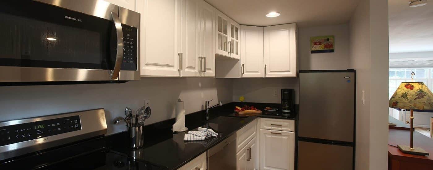 Kitchen area of a studio apartment with black countertops, white cabinets and stainless steel appliances