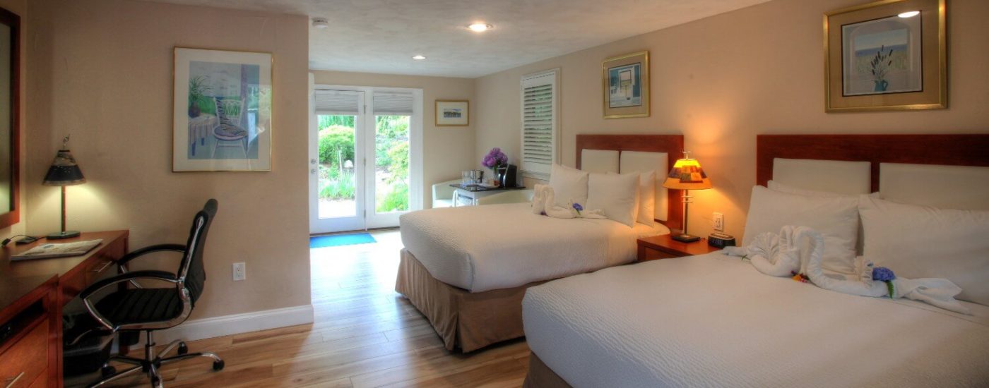 Bedroom with two beds with tall headboards, wood floors, french doors to an outdoor patio, and writing desk with chair