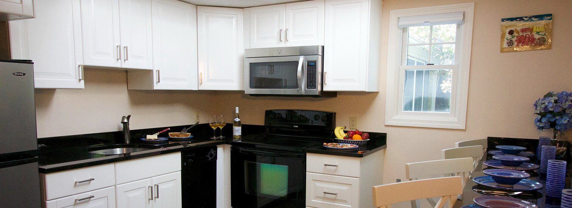 Kitchen with black countertop and white cabinets and bar counter with chairs set with four place settings