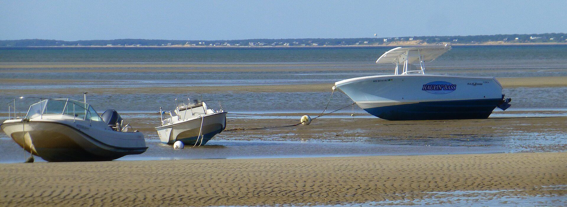 Three boats moored on the beach at waters edge with tide gone out and blue skies overhead