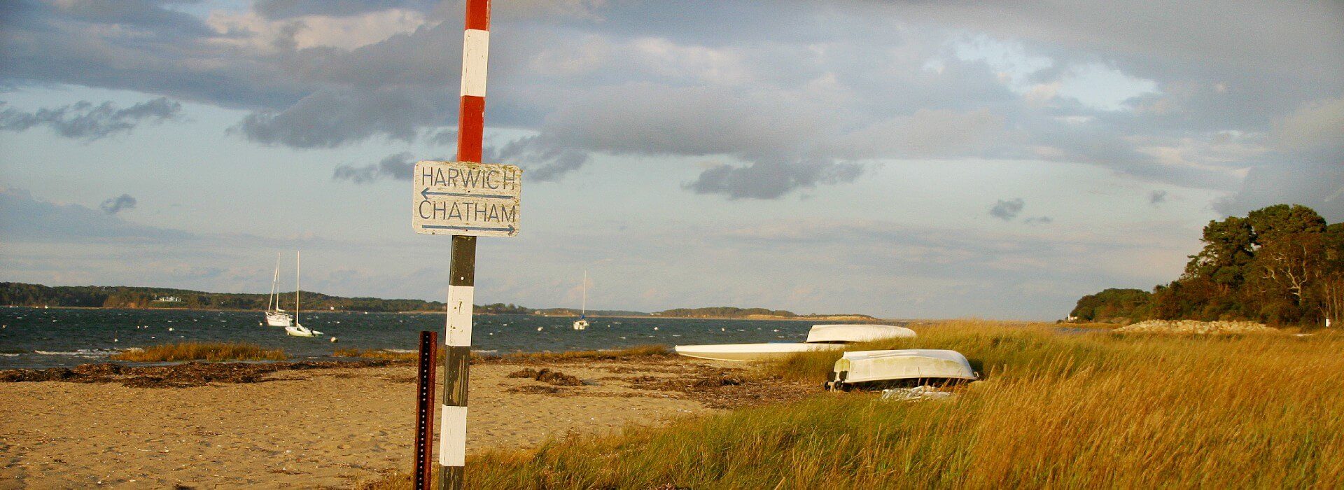 Striped pole with a directional sign for two cities in opposite directions on the beach near dune grass