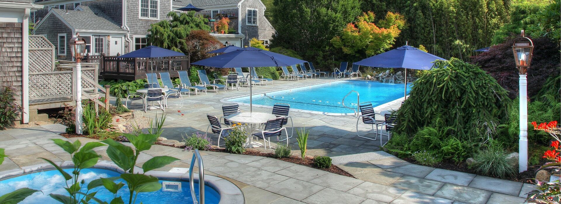 Expansive outdoor patio area with large pool lined with chairs, hot tub, and patio tables with blue umbrellas