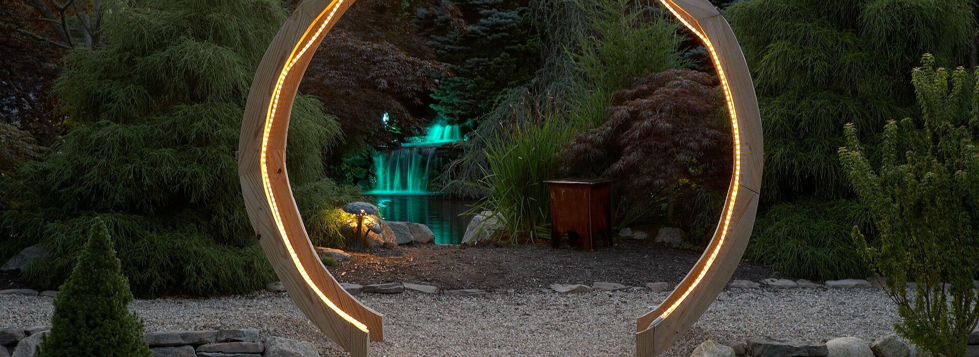 Beautiful wooden circular gate arch lit up by a rope light with view of a waterfall in the background