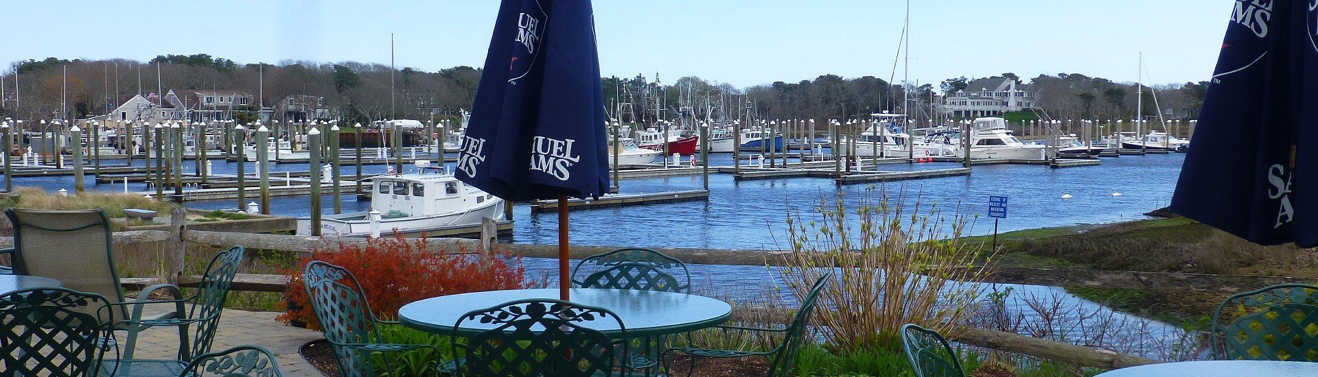 Outdoor patio of a restaurant with several patio tables next to a large marina with boats