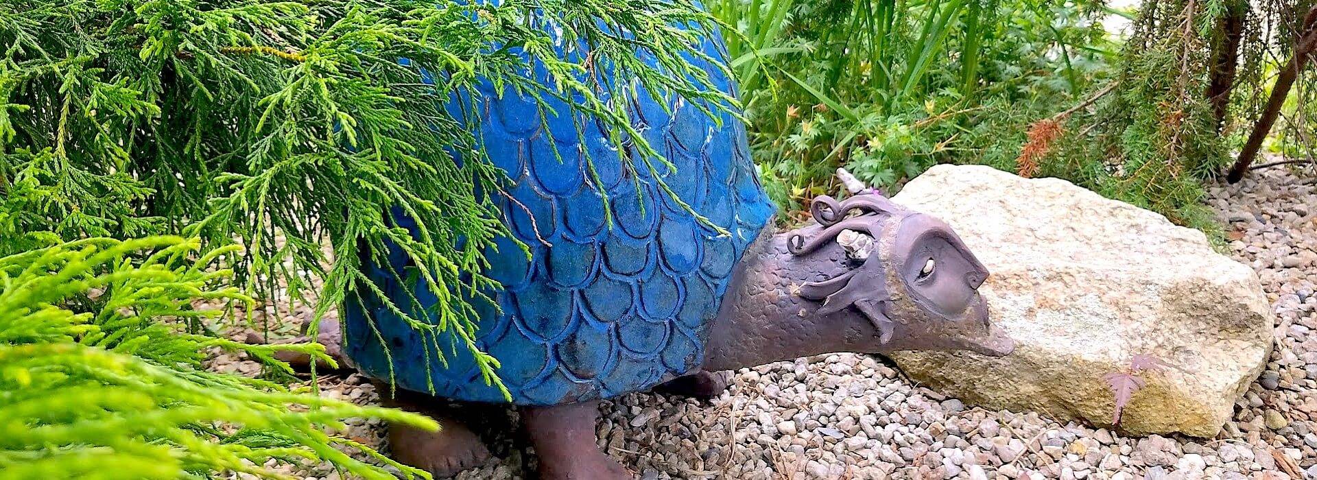 Unique brown and blue metal turtle garden sculpture nestled among rocks and shrubs