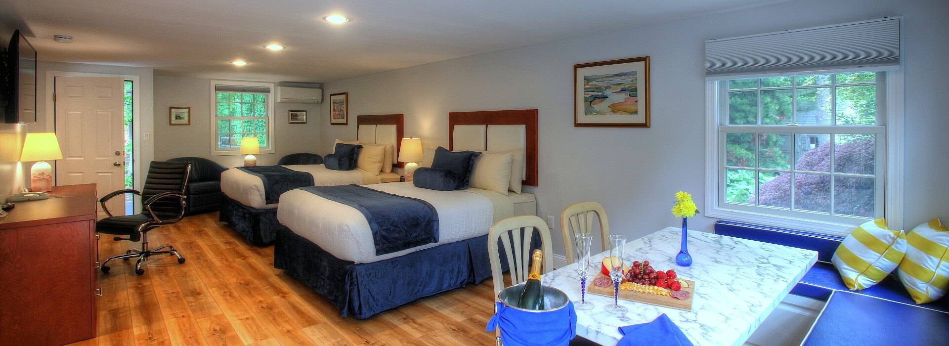 Studio apartment bedroom with two queen beds, dinette under bright windows, dresser and writing desk with chair