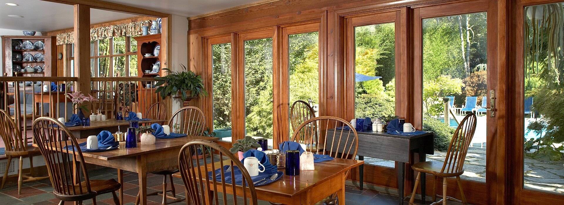 Spacious dining room with a wall of windows overlooking the outdoors and four tables for two set for breakfast